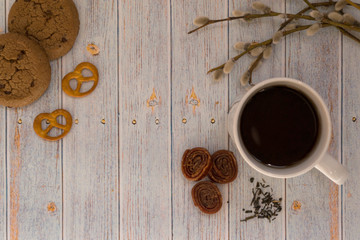 White mug of tea, oatmeal cookies and sweets, with a willow branch on a light wooden background.