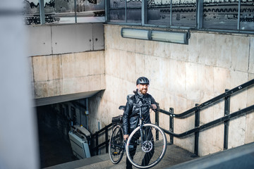 Male courier delivering packages in city, carrying bicycle up the stairs.