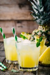 Fresh pineapple juice in two glasses with ice and mint on dark rustic background
