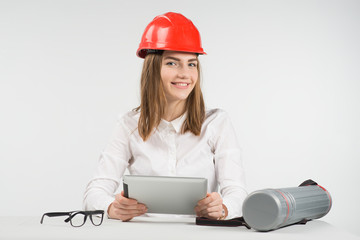 Happy woman architect in orange hardhat holds ipad and sits next to the  tube, glasses