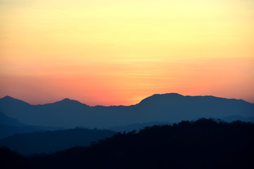 Picture of a sun setting behind a dense forest area followed by mountains