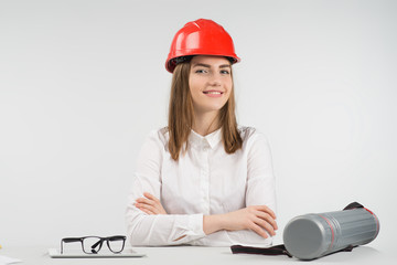 Smiling woman sits at the table in orange hardhat folded her arms