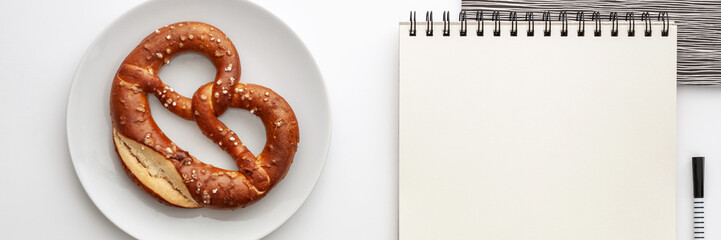Opened empty sketchbook mockup on the desk. Top view real photo. Black-and-white concept desk with pretzel on a white plate. Panorama with place for text