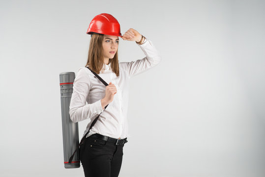 Woman   architect stands with a tube behind her back touches orange helmet on her head. - Horizontal image