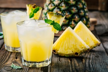 Fresh pineapple juice in two glasses with ice and mint on dark rustic background