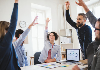Young businesspeople sitting around table in a modern office, celebrating success.