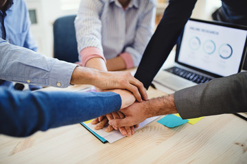 Young businesspeople sitting around table in a modern office, putting hands together.