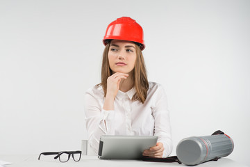 Woman  speculate sits at the table in orange hardhat holds ipad