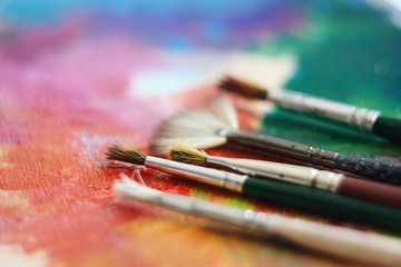 Fototapeta premium Several brushes of different shapes are on a multi-colored palette, painted with oil paints