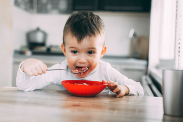 A child in the kitchen eating their own oatmeal with a red plate