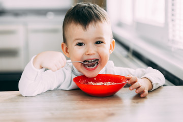 A child in the kitchen eating their own oatmeal with a red plate