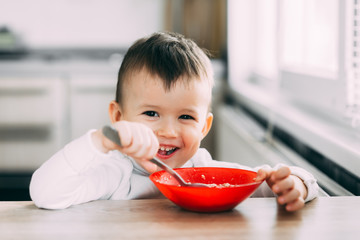 A child in the kitchen eating their own oatmeal with a red plate