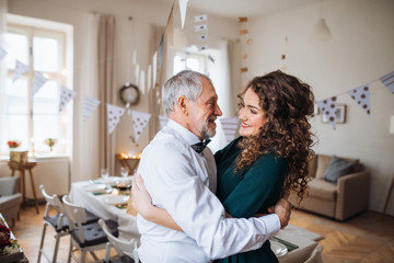 Obraz premium Senior man and young woman standing indoors in a room set for a party, hugging.