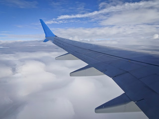 View from the airplane porthole with a wing - flying above the clouds. Aerial cloud landscape.