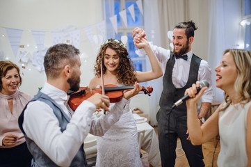 A young bride, groom and other guests dancing and singing on a wedding reception.