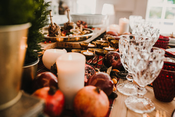 .Detail photograph of a table prepared and decorated for a party diner. Autumnal and festive decoration, with wood pineapples, candles, fruits and red colors. Lifestyle. Food photography