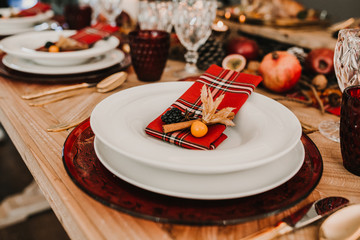 .Detail photograph of a table prepared and decorated for a party diner. Autumnal and festive decoration, with wood pineapples, candles, fruits and red colors. Lifestyle. Food photography