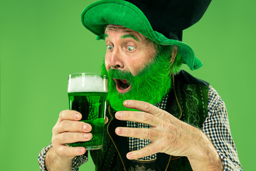A smiling happy senior man in a leprechaun hat with green beer at studio. He celebrates St....