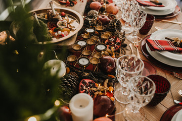.Detail photograph of a table prepared and decorated for a party diner. Autumnal and festive decoration, with wood pineapples, candles, fruits and red colors. Lifestyle. Food photography