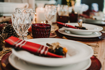 .Detail photograph of a table prepared and decorated for a party diner. Autumnal and festive decoration, with wood pineapples, candles, fruits and red colors. Lifestyle. Food photography