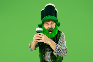 A smiling happy senior man in a leprechaun hat with green beer at studio. He celebrates St....