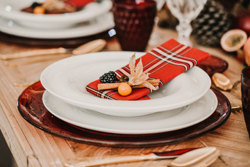 .Detail photograph of a table prepared and decorated for a party diner. Autumnal and festive decoration, with wood pineapples, candles, fruits and red colors. Lifestyle. Food photography
