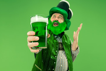 A smiling happy senior man in a leprechaun hat with green beer at studio. He celebrates St....