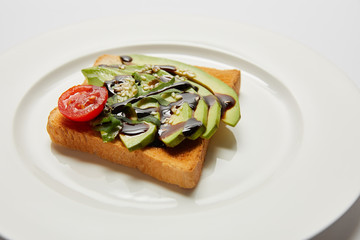 selective focus of toast with avocado and cherry tomato on white plate