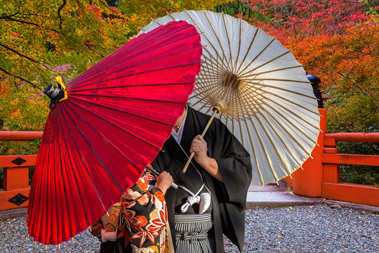 Couple with traditional japanese umbrellas posing at autumnal park in Kyoto