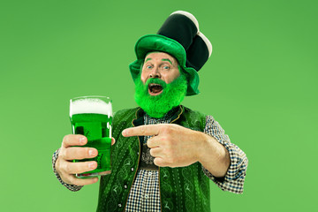 A smiling happy senior man in a leprechaun hat with green beer at studio. He celebrates St....