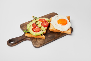 selective focus of wooden cutting board with toasts and scrambled egg on grey background