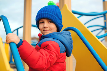 Portrait of happy child outdoors. Cute little boy playing on colorful modern playground. Child have fun in cold time. Happy and healthy childhood. Colorful modern playground. Kids activity outdoors. © volurol