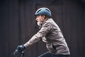 Active senior man with bike helmet cycling outdoors againts dark background.