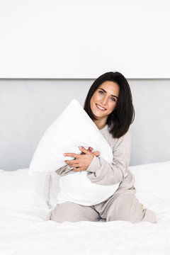 Image of joyful woman 30s laughing, while having fun with pillow in bed at home