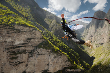 A man in a helmet jumps ropeup with an empty flag in the mountains. Extreme sports. Leisure