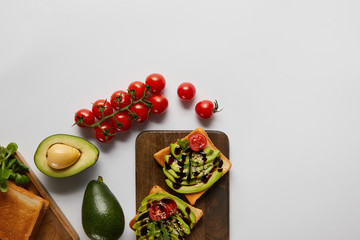 top view of toasts on wooden cutting boards with avocados and cherry tomatoes  on grey backgroud