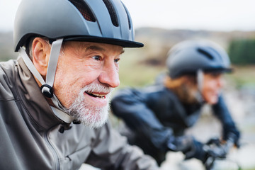 Active senior couple with electrobikes cycling outdoors on a road in nature.