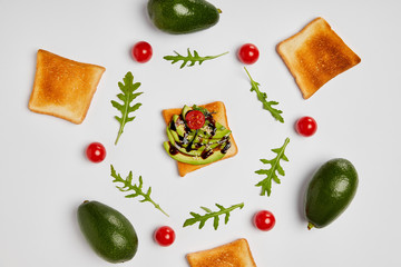 top view of toasts with avocados, cherry tomatoes and arugulas leaves on grey background