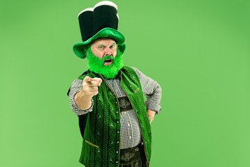 A smiling surprised happy senior man in a leprechaun hat with beard at green studio. He celebrates St. Patrick's Day. The celebration, festive, beer, holiday, alcohol, party, human emotions concept