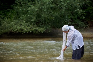 A girl in a long village vintage clothes standing in the river and washes clothes.