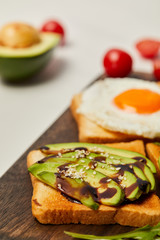 selective focus of cutting board with toasts, scrambled egg, cherry tomatoes and avocado on white background