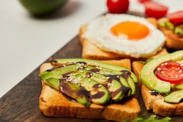 selective focus of cutting board with toasts, scrambled egg, cherry tomatoes and avocado on white background