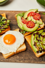 selective focus of toasts with scrambled egg, cherry tomatoes and avocado on wooden background