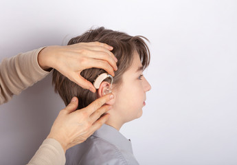 Close up of doctor's hands inserting hearing aid in a youg boy patient's ear