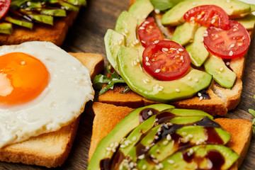 selective focus of toasts with scrambled egg, cherry tomatoes and avocado on wooden background