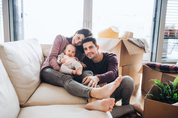 A portrait of young couple with a baby and cardboard boxes moving in a new home.