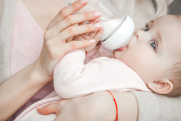 Young mother feeding her little cute baby daughter with bottle of child formula. Woman with her...