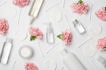 Top view of different cosmetic bottles, carnations flowers, cotton sticks and cosmetic pads on...