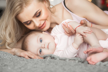 Young mother taking care of her little baby girl. Beautiful mom and her daughter indoors in the bedroom. Loving family. Attractive mum holding her child.