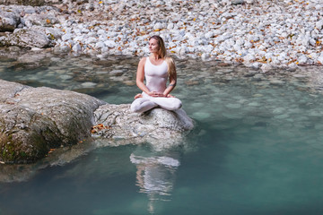 Well-groomed young beautiful girl pilates instructor enjoying the wildlife meditating on stones in the mountains and the river on a warm summer day. Concept of enjoying solitude in nature